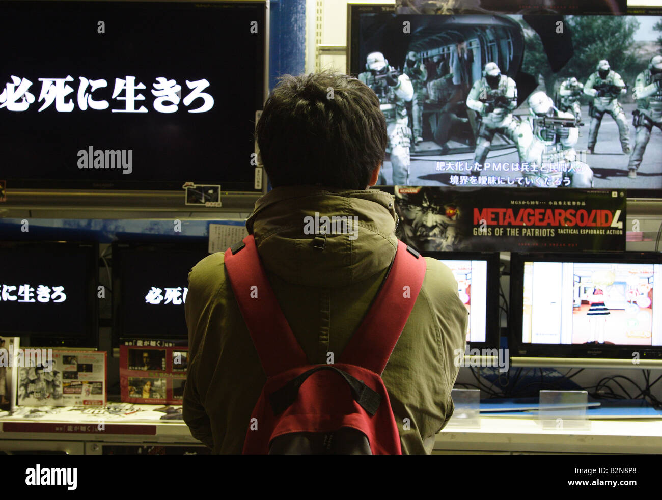A man wearing a backpack watches video game screens in a shop in Akihabara, Tokyo, Japan Stock Photo