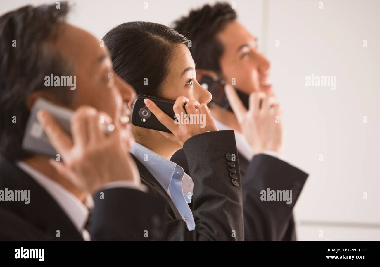 Three business executives using their mobile phones and looking up ...