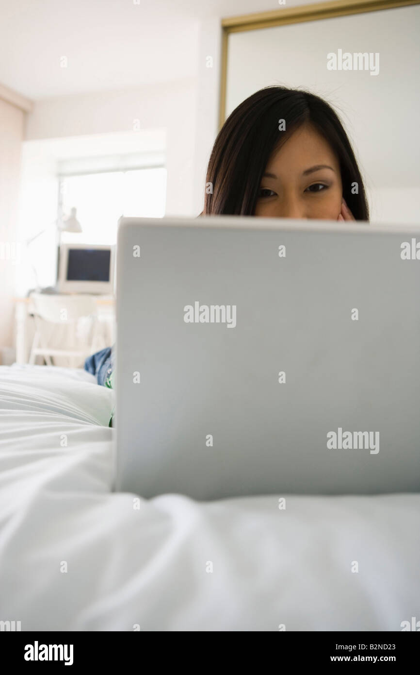 Young woman lying on the bed and using a laptop Stock Photo