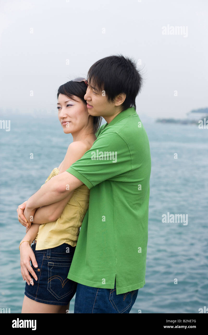 Side profile of a mid adult man embracing a mid adult woman from behind ...