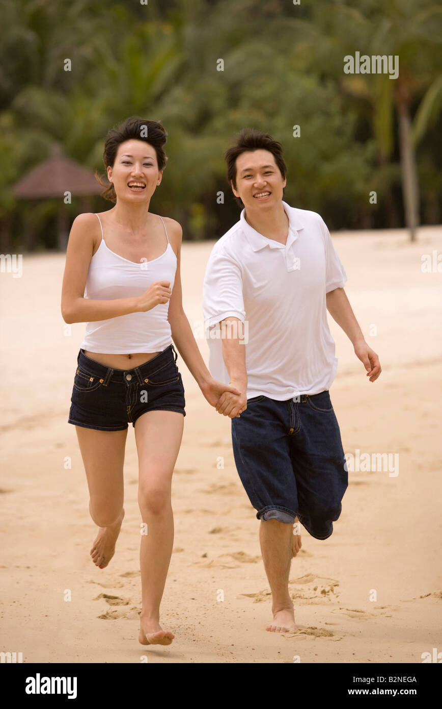 Portrait of a young couple running on the beach Stock Photo - Alamy