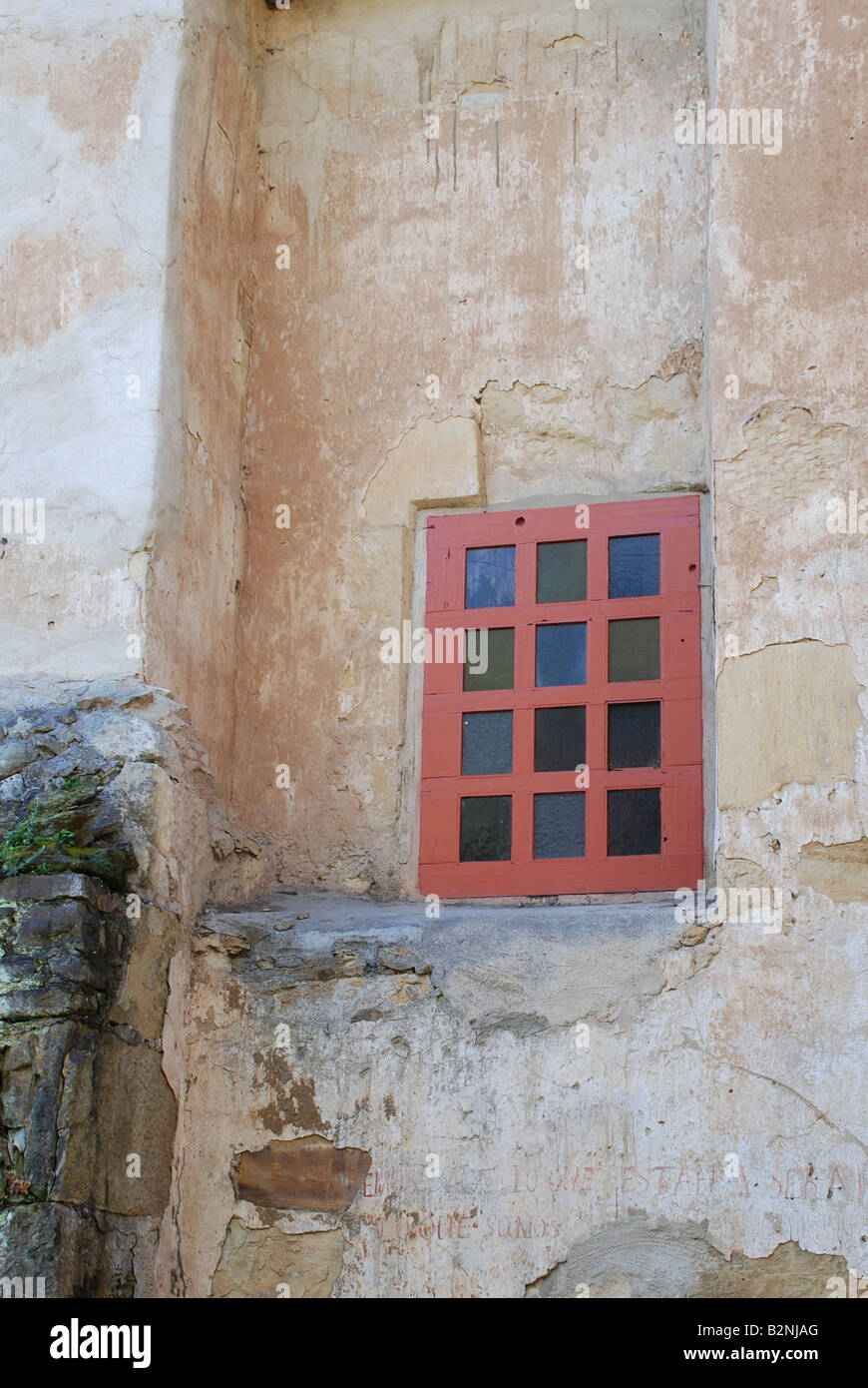Exterior stucco wall with red window frame and colored glass at the Carmel Mission in California