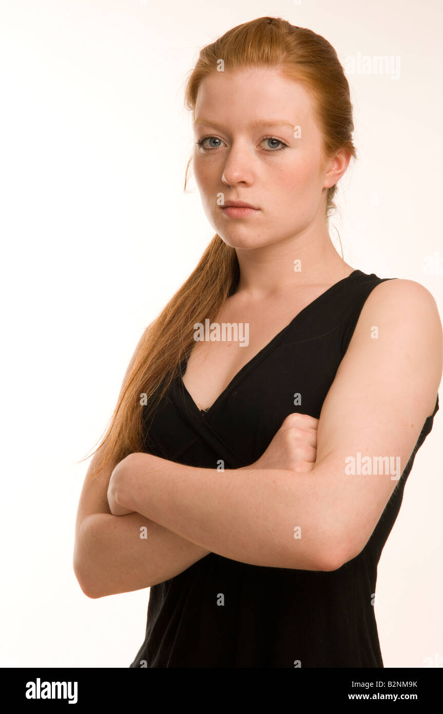 Moody fiery temperamental red haired teenage girl with arms crossed looking aloof and haughty in studio, arms crossed, UK Stock Photo