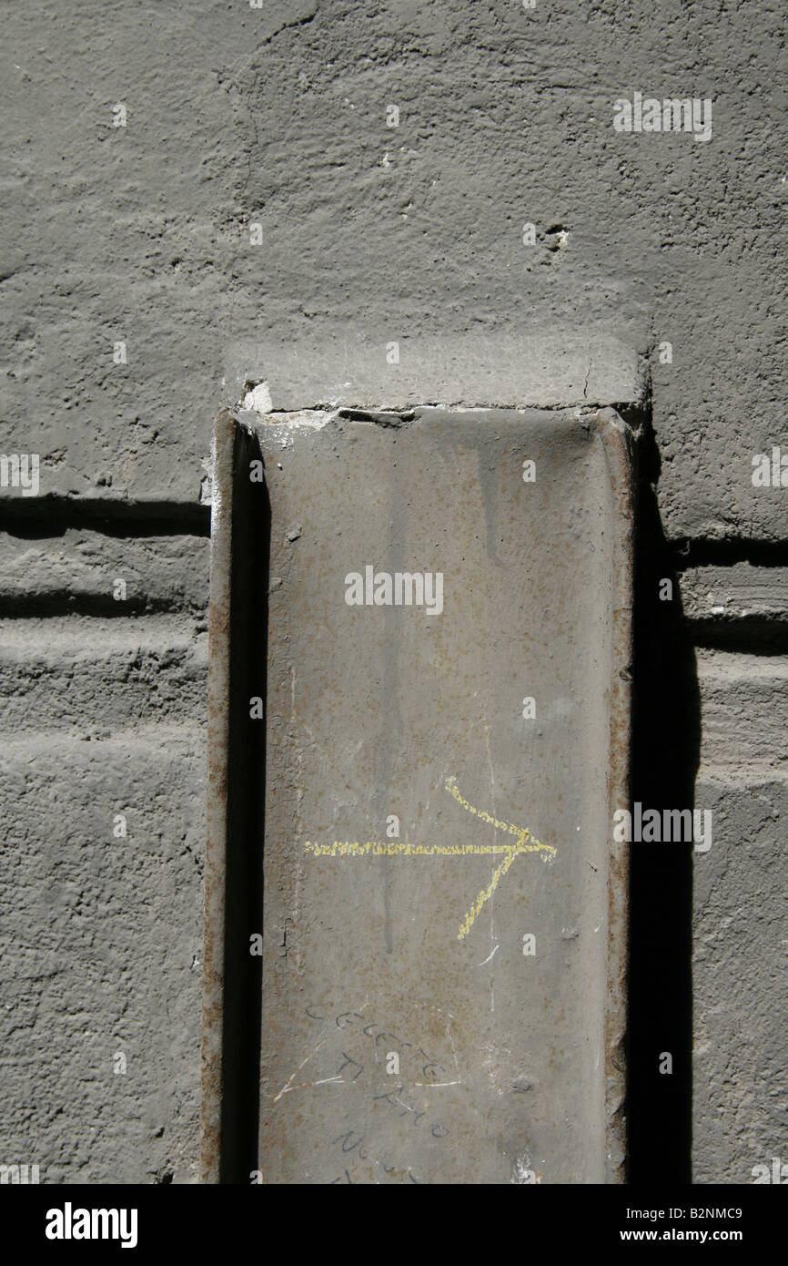 yellow arrow chalk mark on metal beam by dirty wall in sun Stock Photo