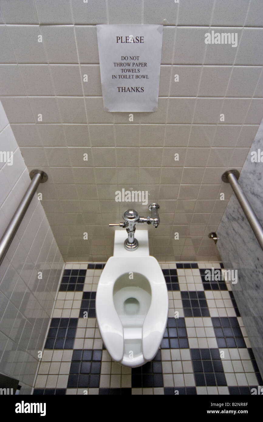 Toilet with sign above it reading Please Do Not Throw Paper Towels In Toilet Bowl Stock Photo