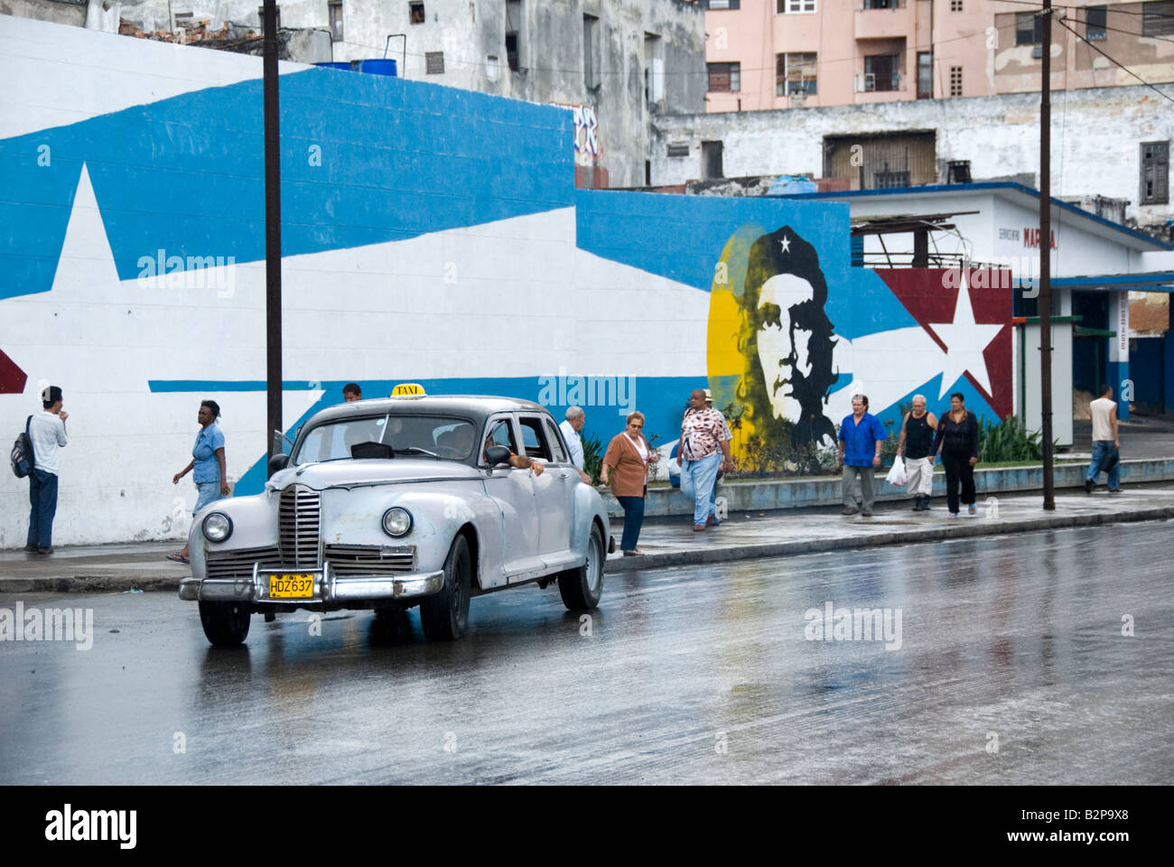 Vintage Taxi cab passing by a mural of Ernesto Che Guevara during time of embargo in Cuba Central Havana Cuba Stock Photo
