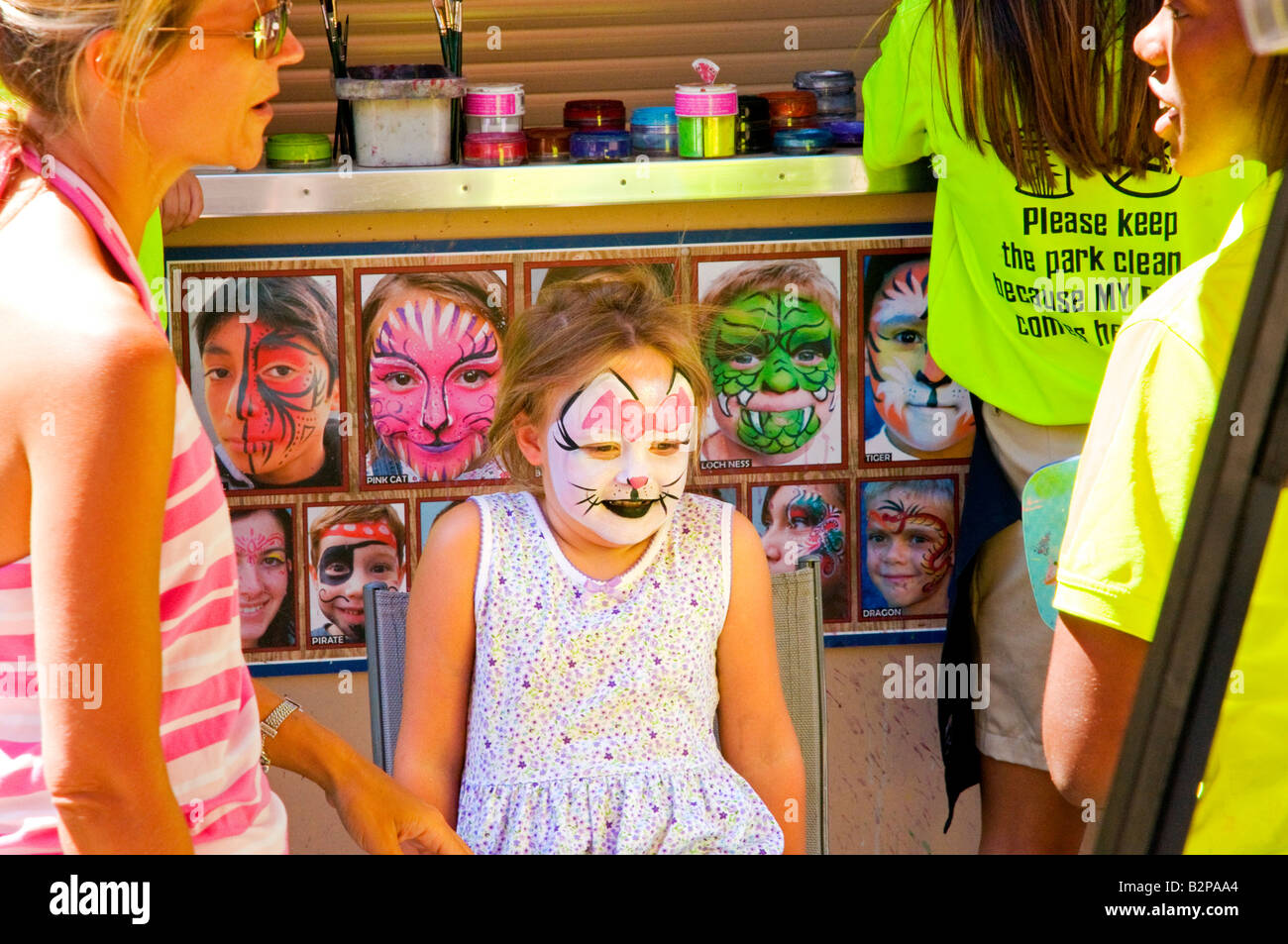 A young girl displays her new cat face paint while her mother talks to artist at Six Flags Great America in Gurnee,Illinois, USA Stock Photo