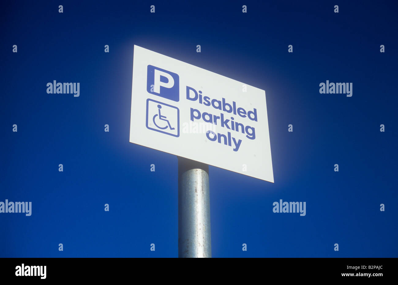 White and blue sign on silver pole with deep blue sky and symbol of person in wheelchair stating P Disabled parking only Stock Photo