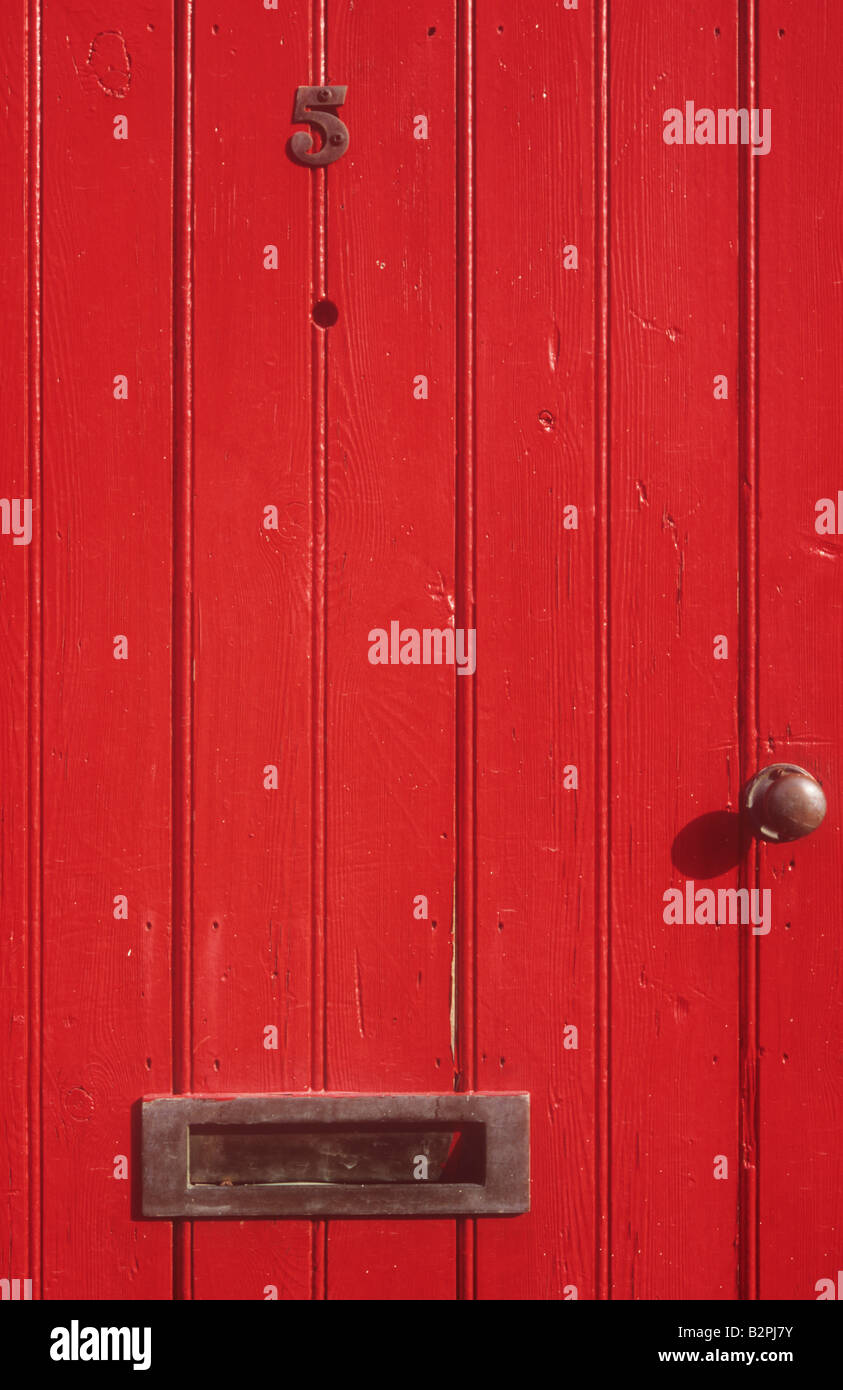 Solid wooden front door painted scarlet red with number 5 letterbox doorknob and peephole Stock Photo