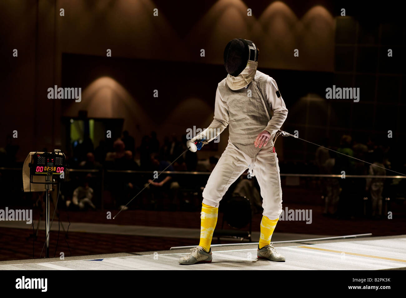 A competitive foil fencer stands ready to begin a fencing bout at a