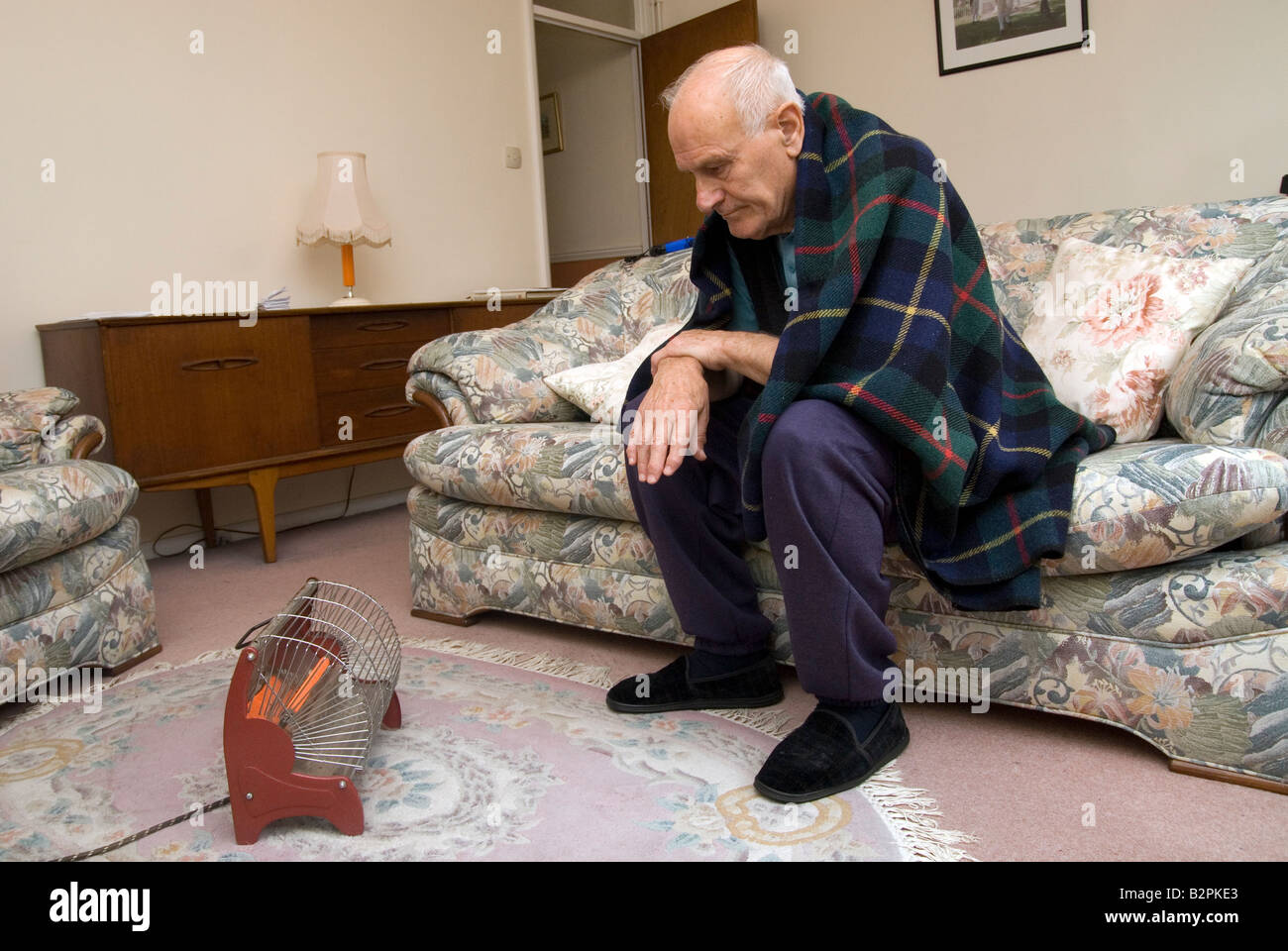 A elderly man keeping warm in front of a electric fire Stock Photo Alamy