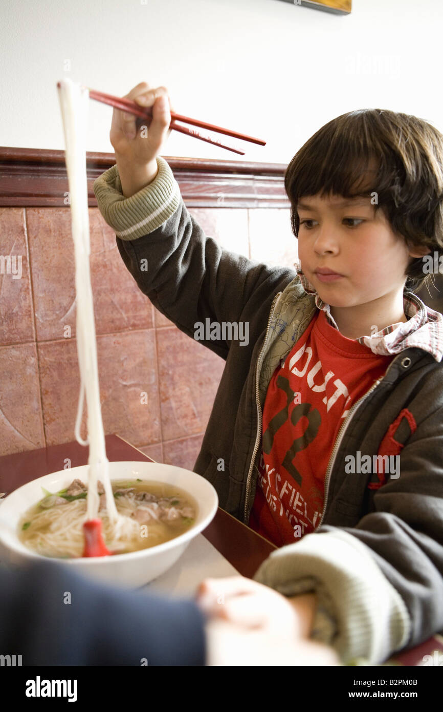 Young boy plays with his noodles while eating a soup in a restaurant