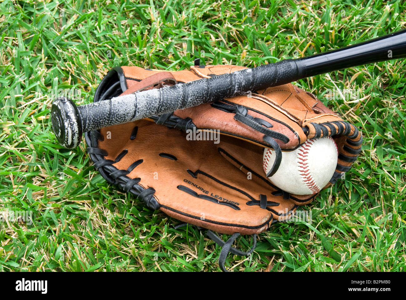 A baseball glove ball and bat lie in the grass before a game Stock