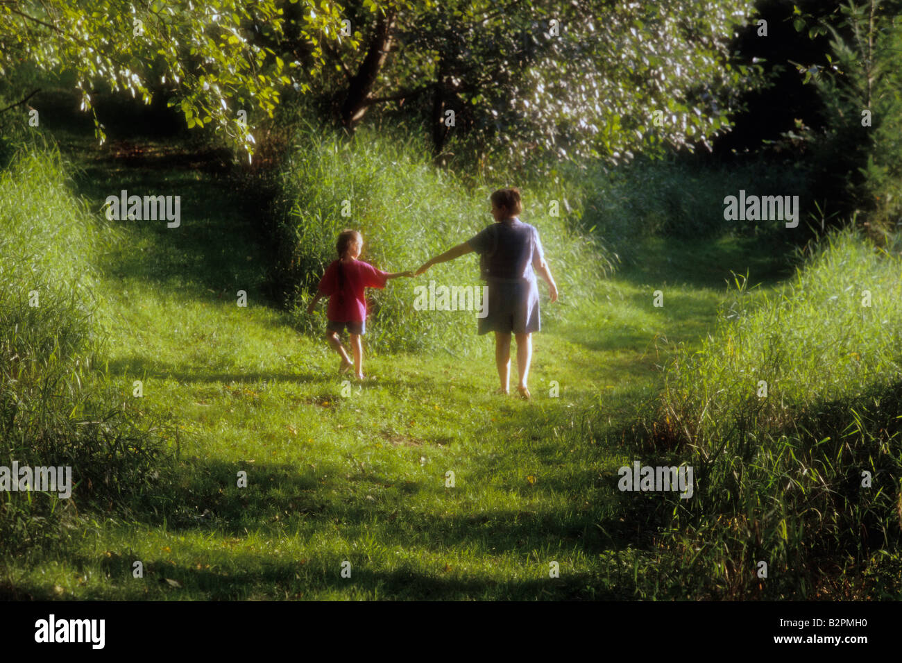 Mother and daughter  walking on a grassy path coming to a crossroad in path Stock Photo