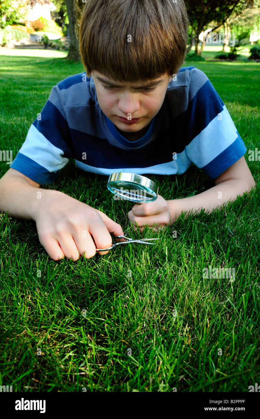 Teenage boy obsessively clipping individual blades of grass with a scissors Stock Photo