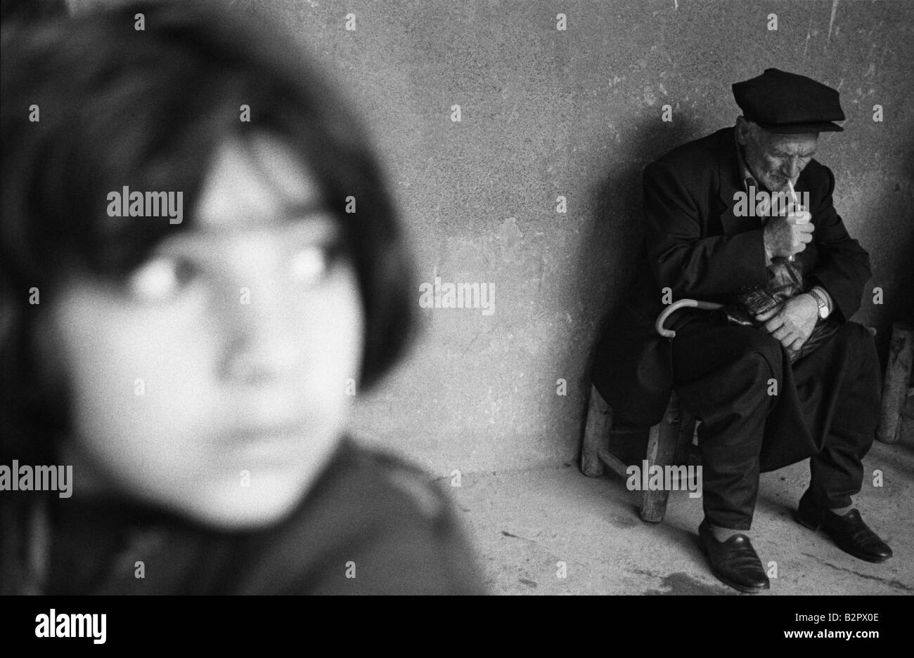 a young kurdish girl looks to the right with a kurdish man in the background lighting a cigarette Stock Photo