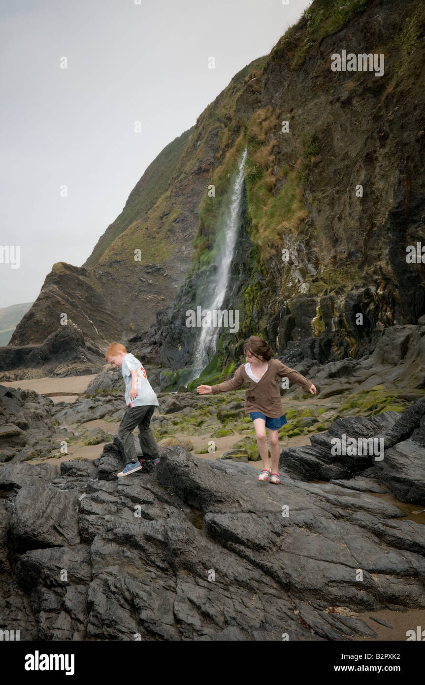 two small children playing on the rocks by the Waterfall on beach Tresaith Ceredigion West Wales UK Stock Photo