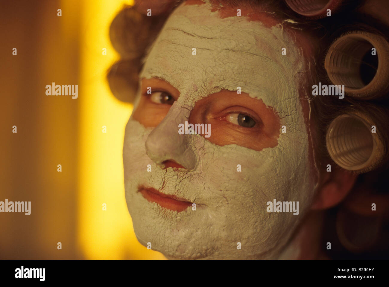 Mature woman wearing a facial mask with hair in rollers looking at