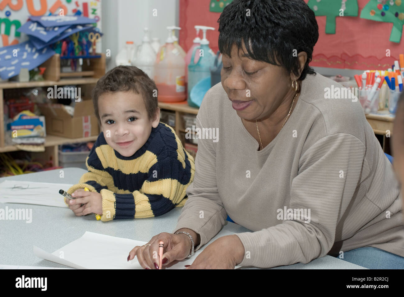 African American preschool teacher helping one of her students to color Stock Photo