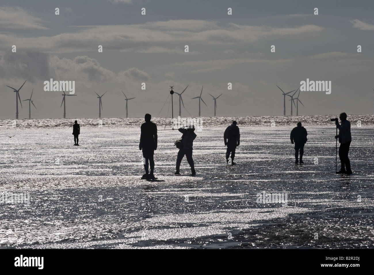 Sculptures by Anthony Gormley's Another Place with windmills in the background Photographers near by Crosby Beach Liverpool UK Stock Photo