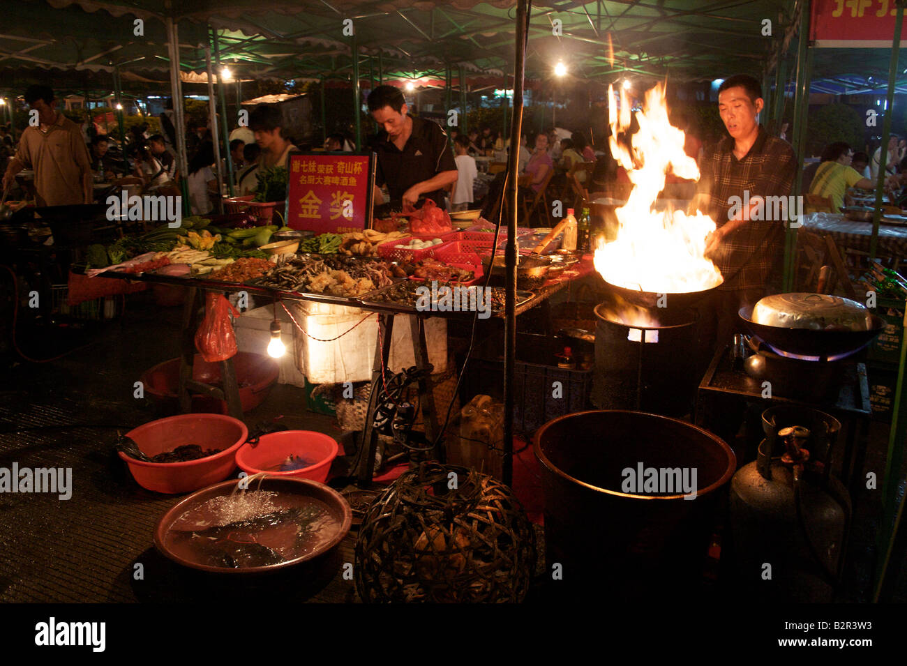 Open air restaurant with a cook wielding a flaming wok and fresh  ingredients on display at night Yangshuo Guangxi China Stock Photo - Alamy