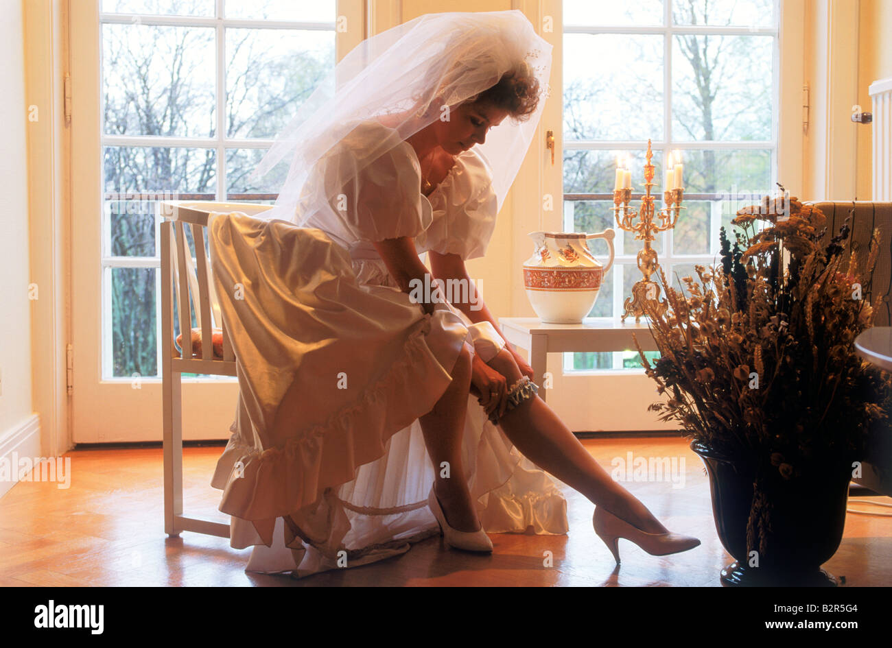 Bride in beautiful wedding gown adjusting garter on leg in soft light