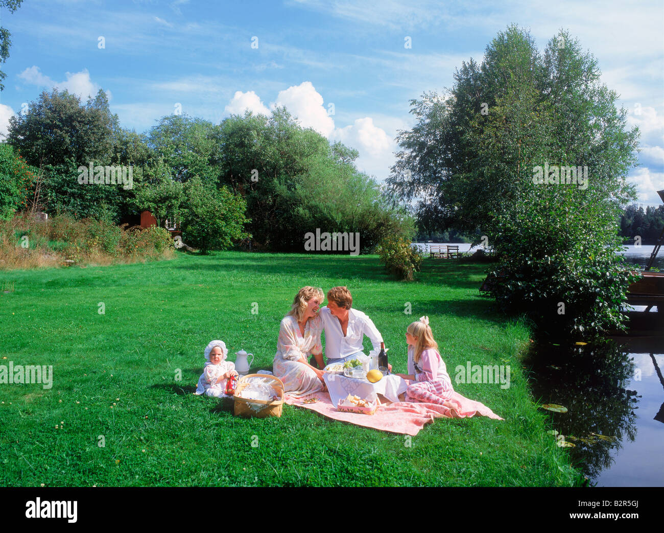 Family of four having summer picnic near lake on grassy
