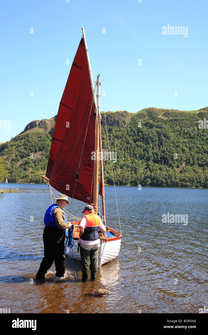 Retired couple preparing a white sailing boat with red sail on Ullswater, The Lake District National Park, Cumbria, England, United Kingdom. Stock Photo