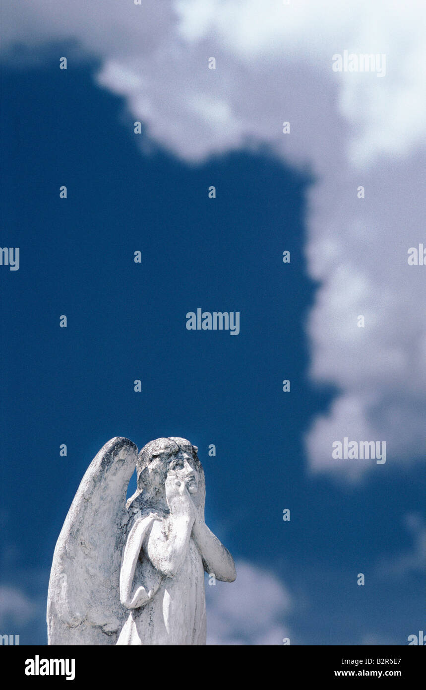 White sculpture of an angel with its hands on its face looking up at the heavens, on a gravestone in Cuba Stock Photo