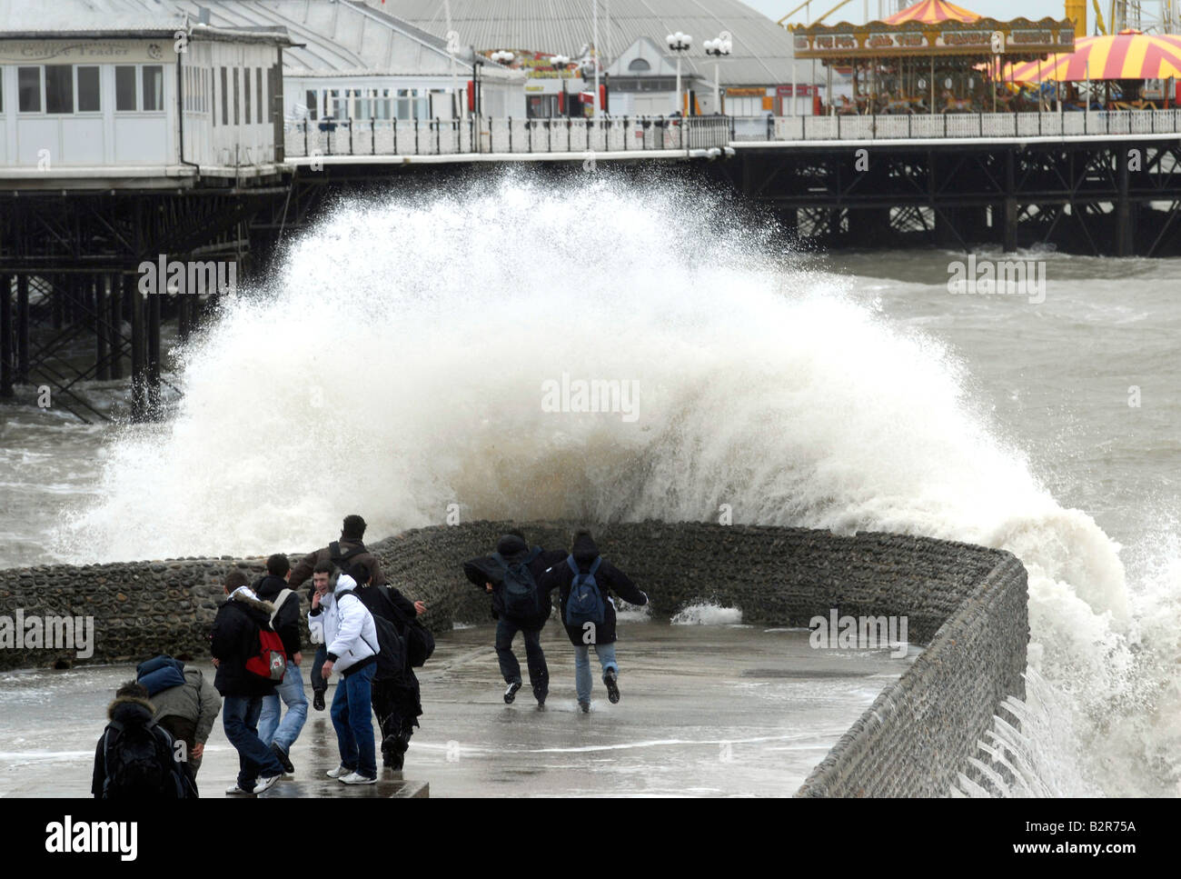 Young people chasing waves on a jetty by Brighton Pier, formerly Palace Pier, during a winter storm, Brighton, UK Stock Photo