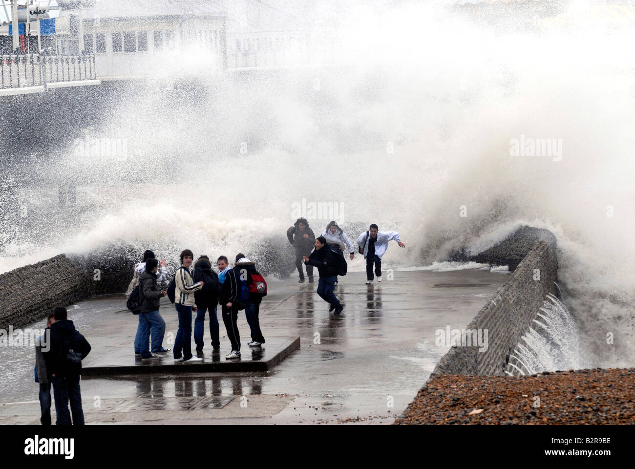 Young people chasing waves on a jetty by Brighton Pier, formerly Palace Pier, during a winter storm, Brighton, UK Stock Photo