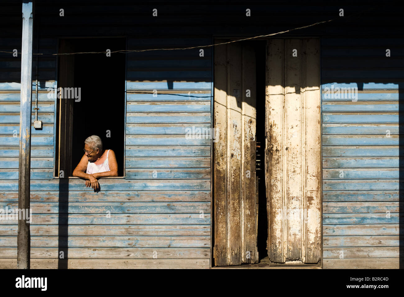 An elderly woman looks through the window of her home in Baracoa Cuba Stock Photo