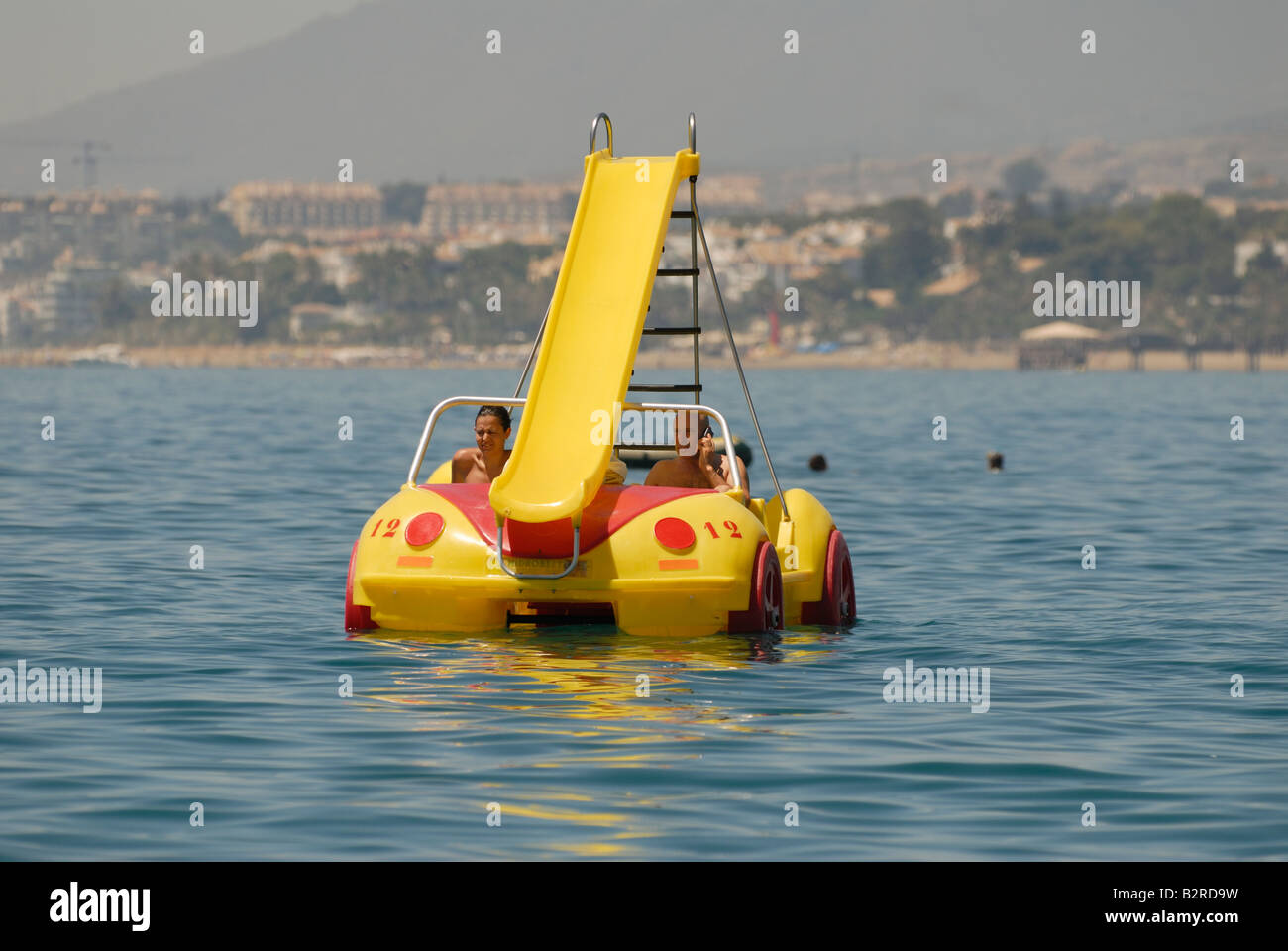 Man and a woman in VW Beetle shaped pedal boat with slide attatched, with man talking on mobile phone Stock Photo