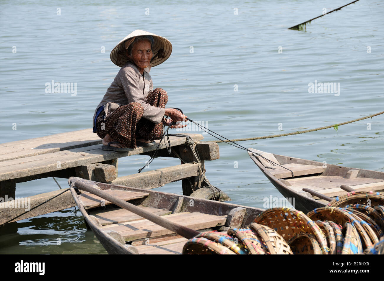 Agile elderly Vietnamese woman tying her wooden boat after a days work Hoi An Harbour Vietnam Stock Photo