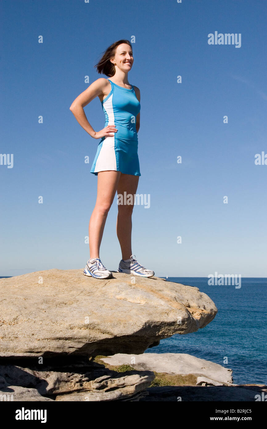 Female Runner in Blue Dress on Rocky Ledge by Sea Stock Photo