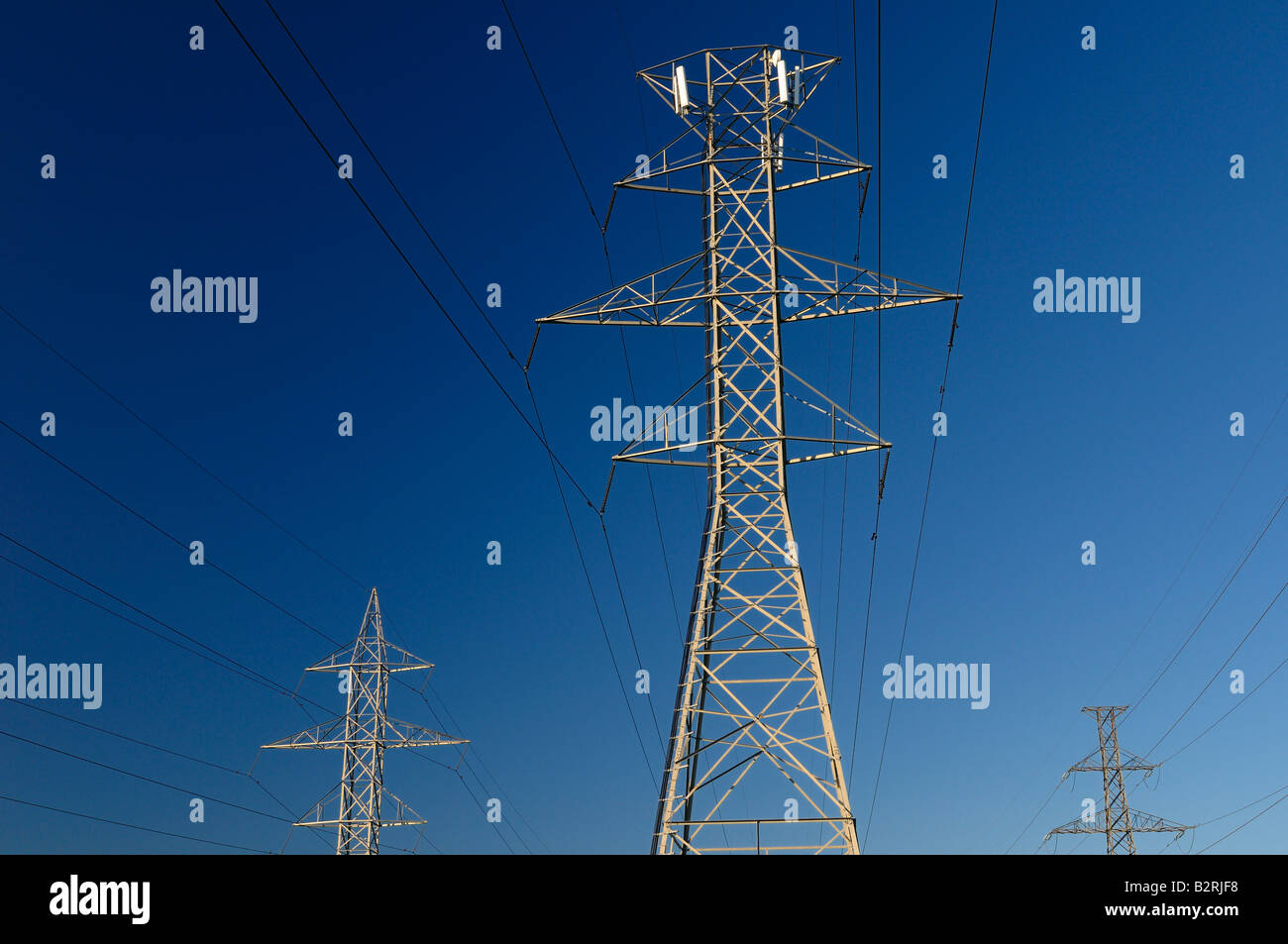 Cell phone telecommunication transmitters on one of three steel frame hydro towers against a blue sky Toronto Stock Photo