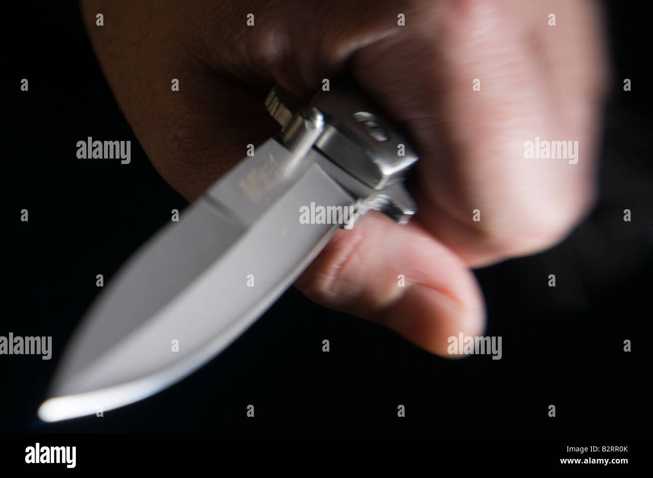Hand holding knife blade against dark background Stock Photo