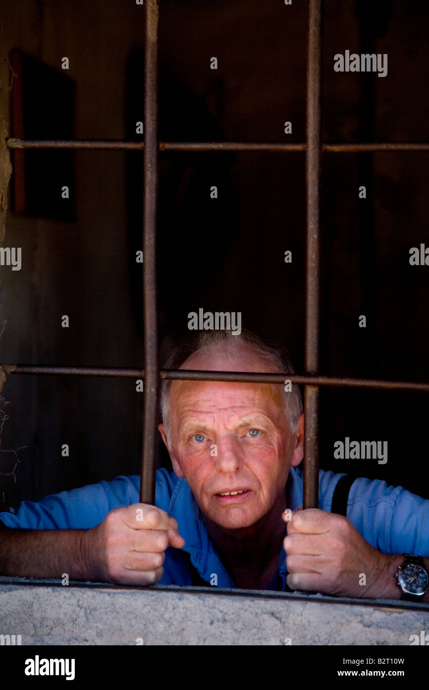Older man looking out from behind jail cell holding the cell bars Stock Photo