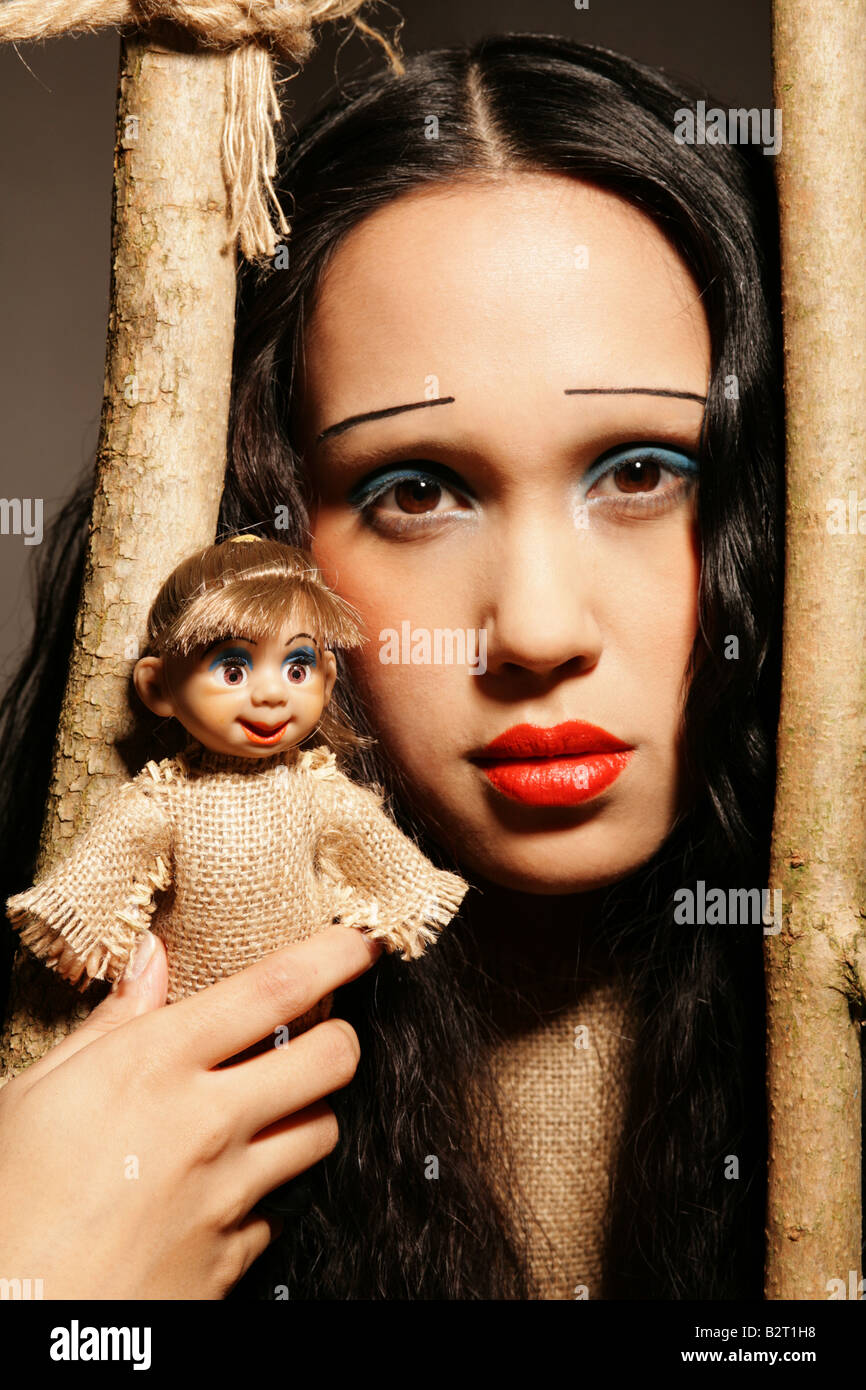 Portrait of young woman of Philippine origin with girlie make up manga make up in a dress behind bars holding a puppet Stock Photo