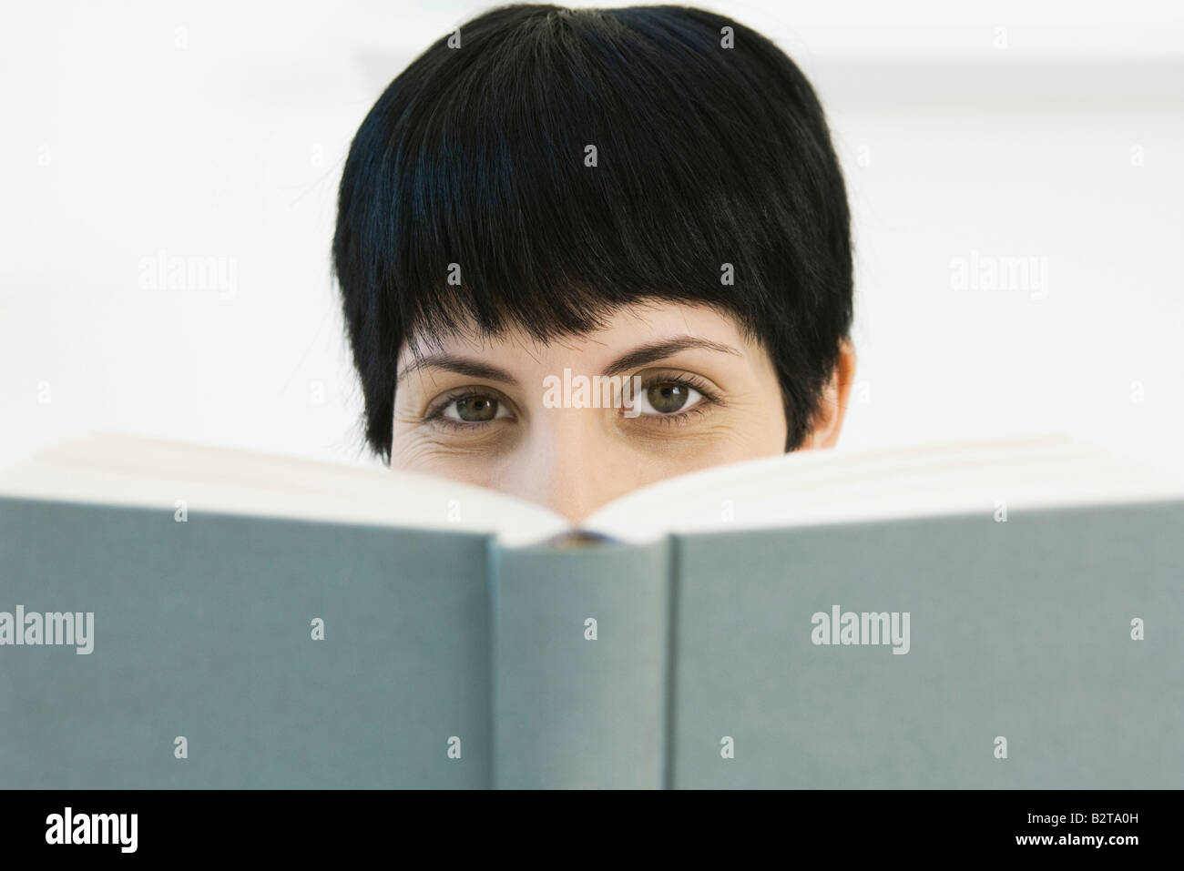 Woman peering over book at camera Stock Photo