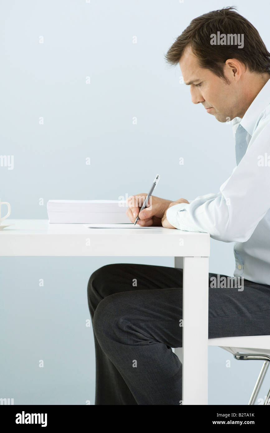 Man sitting at table, writing, side view Stock Photo - Alamy