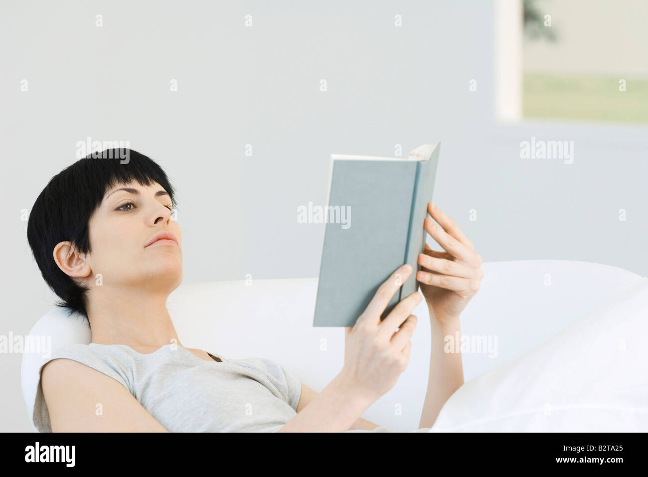 Woman reclining in chair, reading book Stock Photo