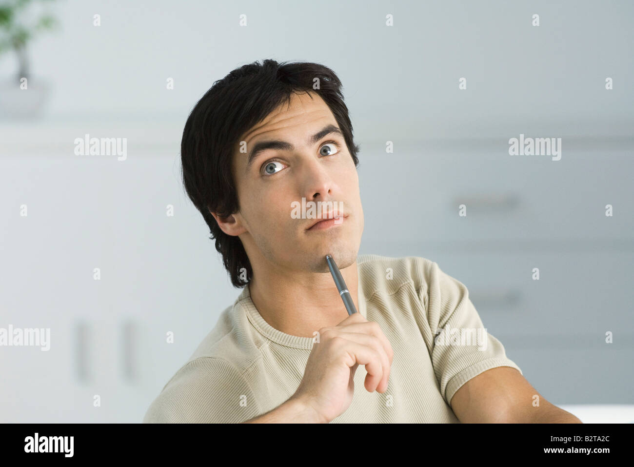 Man looking up, holding pen to his chin, raising eyebrows Stock Photo