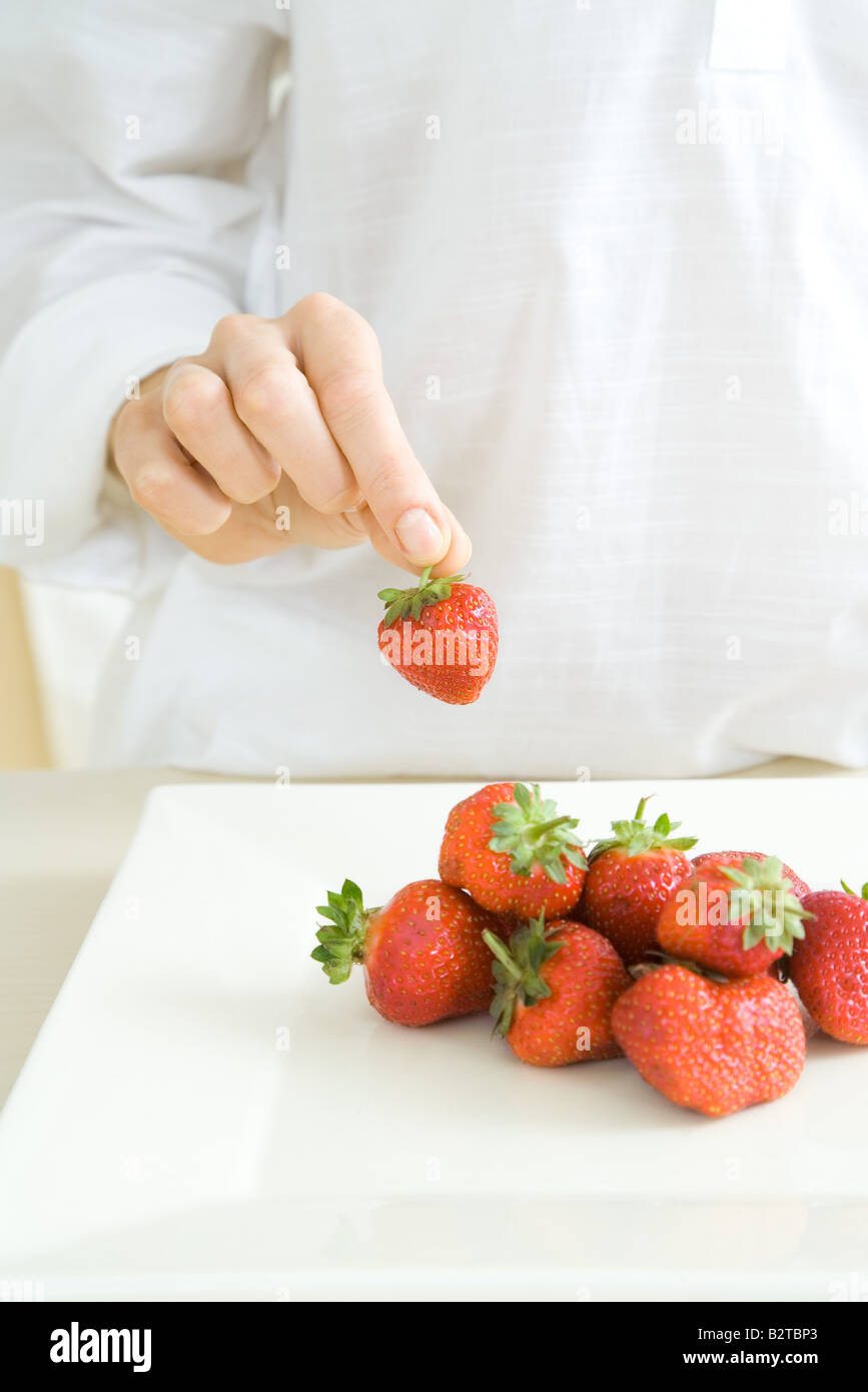 Hand picking up a strawberry from a pile on the counter Stock Photo