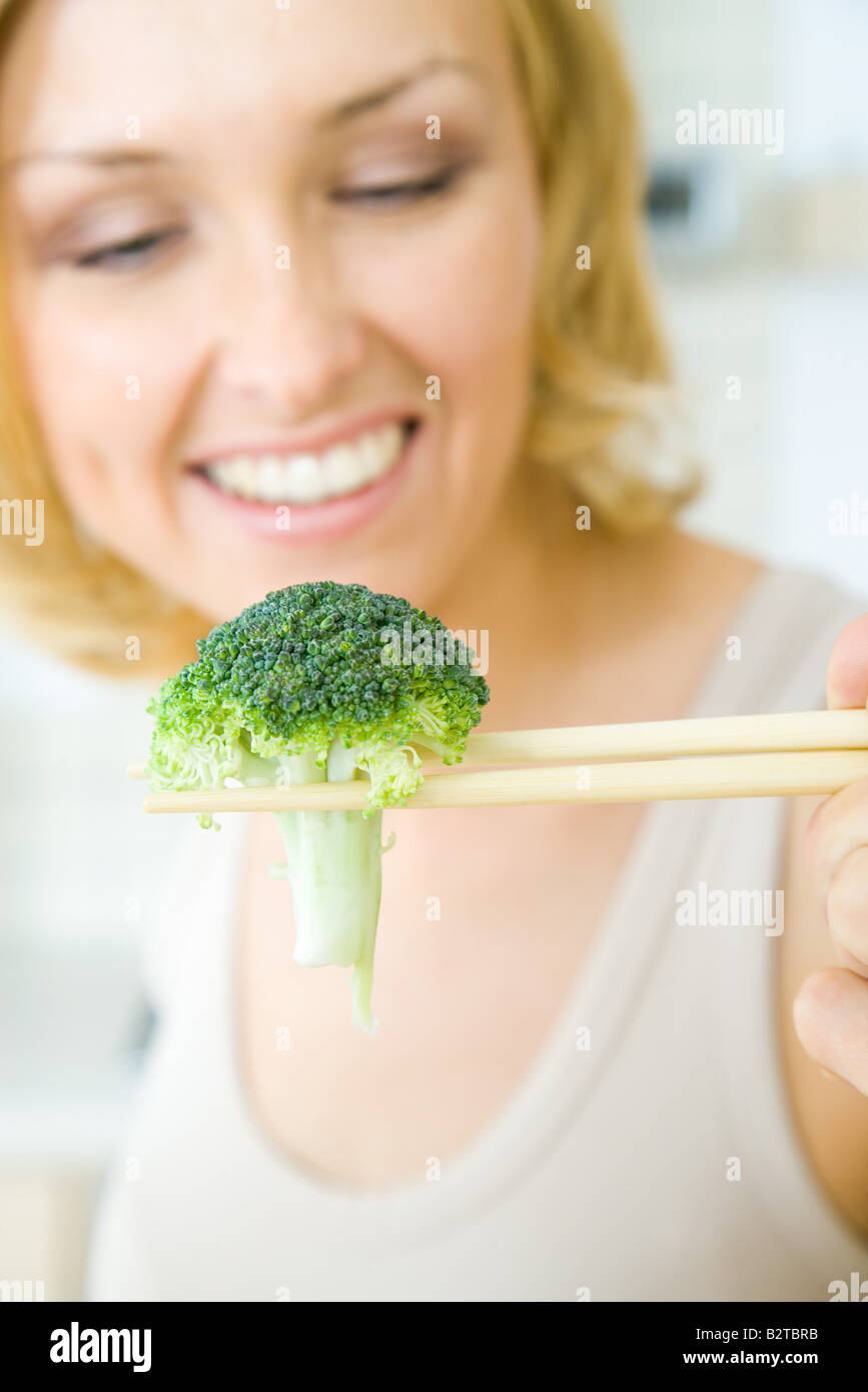 Woman using chopsticks to hold a single piece of broccoli, focus on foreground Stock Photo