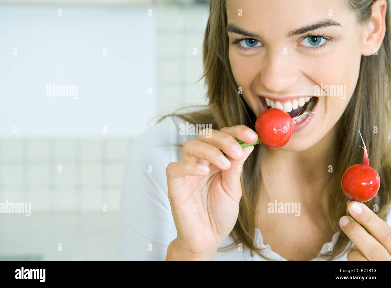 Young woman biting into a radish while holding another, smiling at