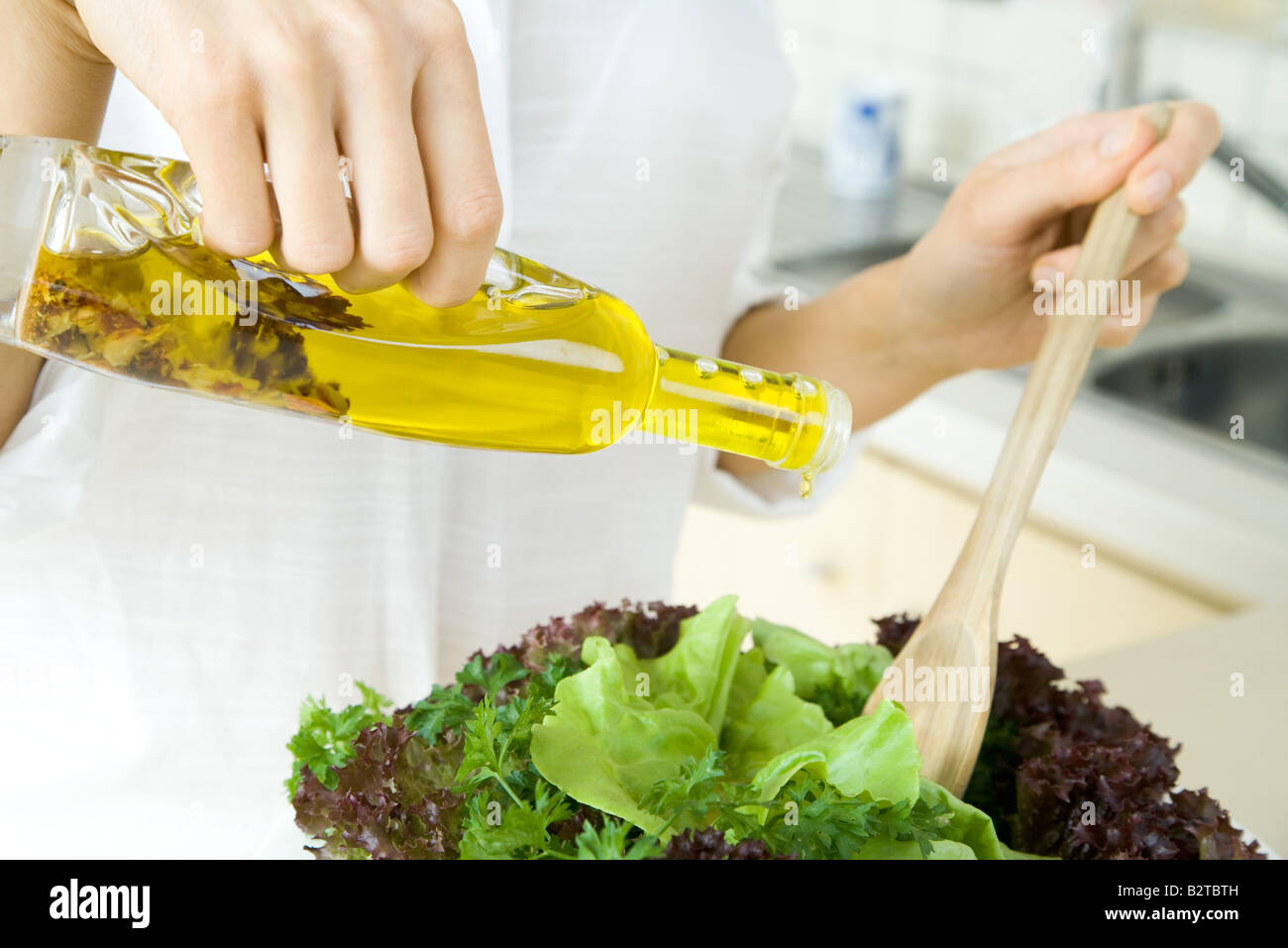 Woman pouring olive oil dressing over salad, cropped view Stock Photo