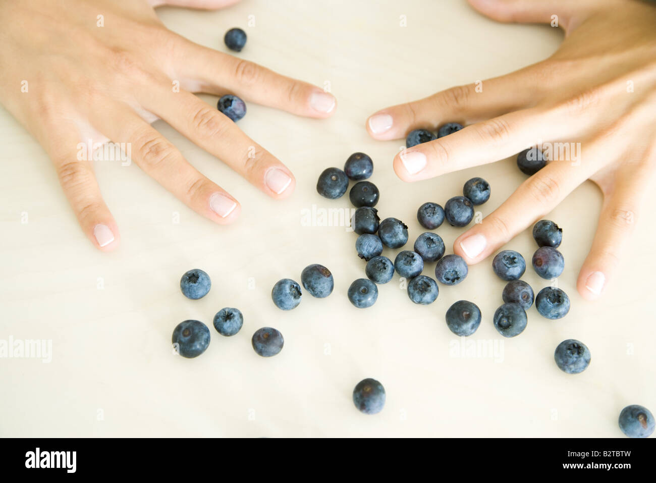 Pair of hands with fingers spread wide open above scattered blue berries Stock Photo