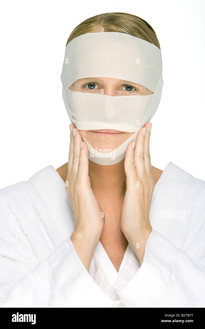 Woman with bandaged face, touching cheeks, looking at camera Stock Photo