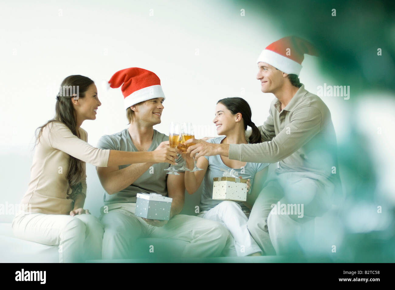 Two couples toasting and exchanging gifts, men wearing Santa hats Stock